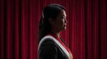 Silueta de mujer con cabello oscuro recogido, banda presidencial de Perú y chaqueta oscura. Fondo de telón rojo.