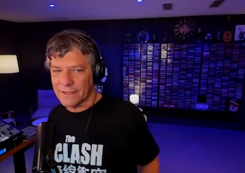 Mario Pergolini viste una camiseta negra con auriculares y habla ante un micrófono en un estudio rodeado de discos