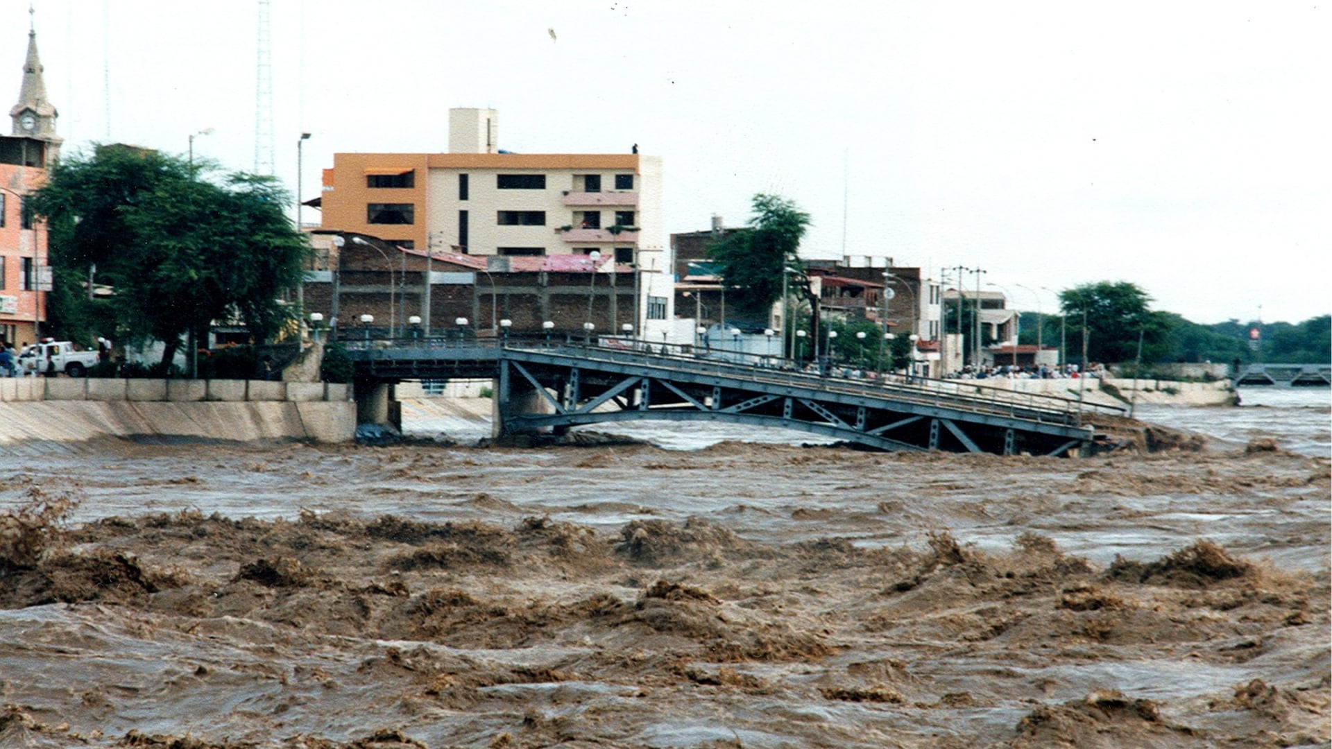 El río Piura desbordado, con el puente Sánchez Cerro parcialmente sumergido y estructuras edilicias afectadas por el