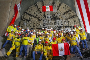 Un grupo grande de trabajadores con cascos y chalecos amarillos posa frente a la tuneladora "Delia", decorada con una bandera de Perú, dentro del túnel excavado