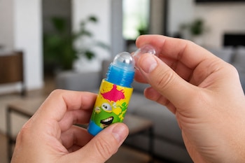 Manos de una persona sostienen una pequeña botella de plástico de colores con una tapa transparente y una esfera en la punta.