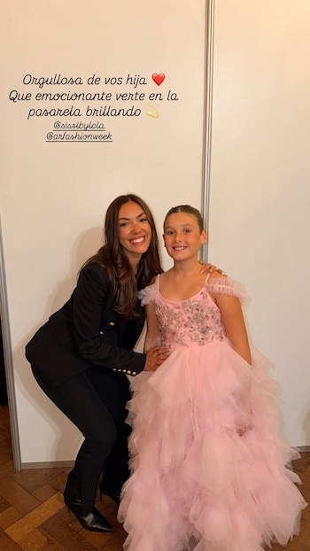 Floppy Tesouro con traje negro sonríe junto a su hija Moorea, vestida con un traje rosa de tul, ante una pared blanca