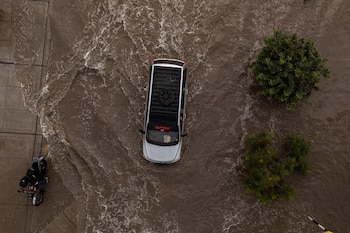 Vista aérea de una camioneta gris y una motocicleta que circulan por una calle inundada de agua marrón junto a dos árboles