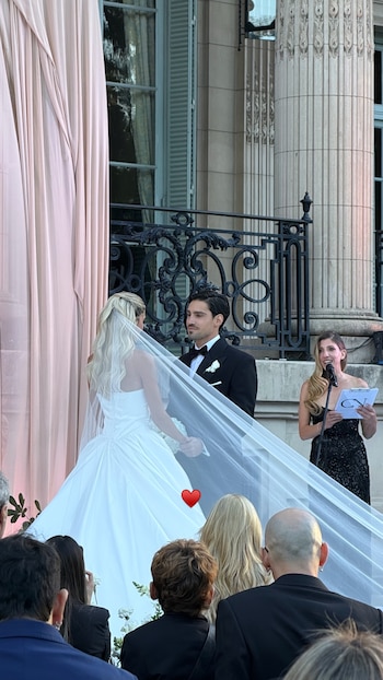 Cande Ruggeri en vestido de novia y velo, de espaldas, mira a Nico Maccari en esmoquin. Oficiante con micrófono. Exterior del Palacio Sans Souci