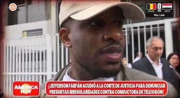 Primer plano de Jefferson Farfán, hombre de piel oscura, gorra beige y polo blanco, hablando al aire libre. Hay otras personas y un edificio detrás. Un banner rojo con texto cubre parte inferior