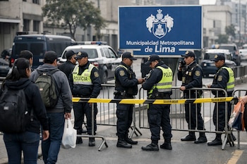 Policías con chalecos reflectantes controlan un perímetro con vallas y cinta amarilla de seguridad en una avenida. Hay un cartel de la Municipalidad de Lima y personas.