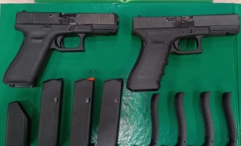 Dos pistolas semiautomáticas negras, seis cargadores de arma, uno con punta naranja, y cuatro culatines de empuñadura sobre superficie verde
