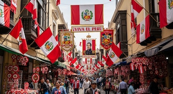 Calle con banderas de Perú, estandartes patrios, retrato de un prócer y tiendas que venden escarapelas. Numerosas personas caminan en el centro de la vía.
