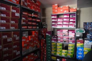 Múltiples estanterías metálicas llenas de cajas de zapatos de colores como rojo, naranja, morado, verde y azul, con marcas como Nike, Vans y Adidas