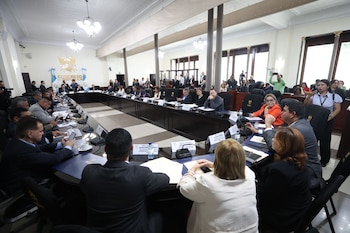 Decenas de personas en trajes sentadas alrededor de una larga mesa en una sala de reuniones del Congreso de Guatemala. Se ven micrófonos y documentos
