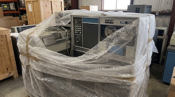 Un equipo informático IBM 1401 cubierto con plástico de burbujas en un depósito con cajas de madera.