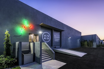 Vista exterior nocturna de El Espacio 23, un edificio gris oscuro con una instalación de luces de neón verde y rojo, escaleras y rampas de acceso