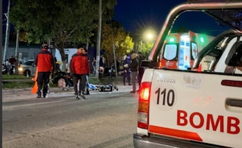 Escena nocturna en una calle con un camión de bomberos blanco y una ambulancia, personal de emergencia y una motocicleta en el suelo
