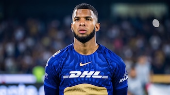 Un futbolista con barba corta viste una camiseta deportiva de color azul con el logotipo de DHL sobre un fondo desenfocado.