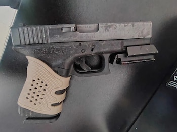 Una pistola semiautomática de color negro con empuñadura de goma beige reposa sobre una superficie oscura y plana