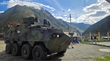Vehículo blindado camuflado con ocho ruedas y marca Hyundai Rotem en su lateral, estacionado frente a una cadena montañosa bajo un cielo nublado