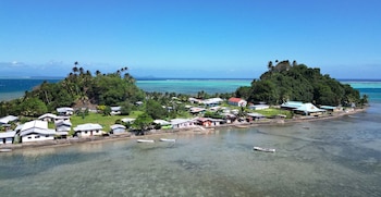 Vista aérea de casas bajas junto a la orilla del mar en una isla rodeada de colinas verdes y botes sobre aguas transparentes