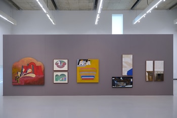 Una pared de galería gris exhibe siete obras de arte abstracto vibrantes en diferentes tamaños y estilos, con formas geométricas, texto "A & A" y texturas