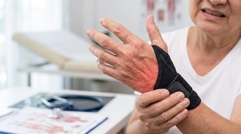 Mano con una muñequera negra y tono rojo en la piel, sostenida por la otra mano sobre un escritorio con estetoscopio.