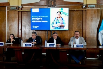 Un hombre habla en un podio frente a una pantalla que muestra mapas de Guatemala con cifras de aperturas de farmacias de 2024 a 2026