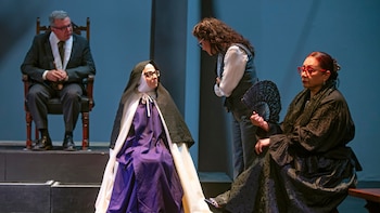 Cuatro personas sobre un escenario con vestimentas de monja, traje oscuro y vestido tradicional con abanico