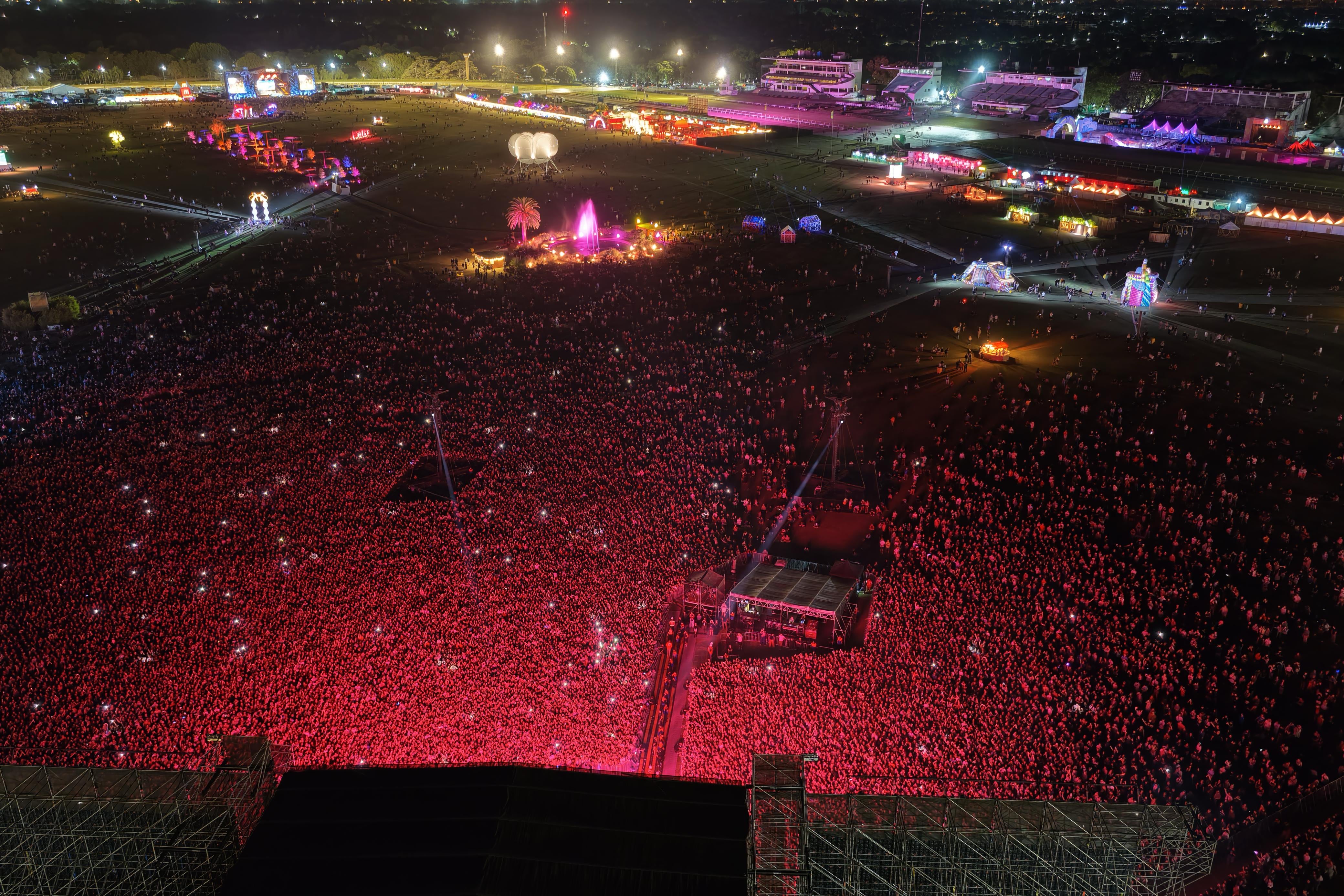 Una multitud vibrante asiste al festival Lollapalooza Argentina por la noche, donde luces rojas iluminan a miles de personas en un ambiente festivo.