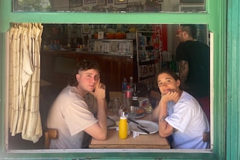 Hombre y mujer, Lucas Vignale y Delfina Pignatiello, sentados en una mesa de restaurante con platos, botellas y dispensador de mostaza