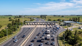 Una autopista de varios carriles con automóviles y camiones que se aproximan a una estación de peaje en una zona rural