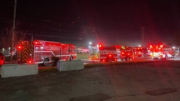 Varios camiones de bomberos rojos con las luces traseras encendidas en un estacionamiento asfaltado durante la noche
