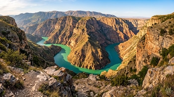 Un río de color verde turquesa fluye en un cañón profundo rodeado de altas montañas y paredes de roca estratificada.