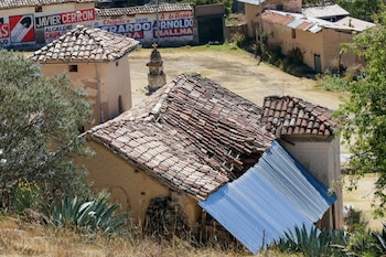 Tejado de tejas de barro de una construcción dañado, cubierto parcialmente con una lámina de metal azul. Vegetación seca, muros de adobe y carteles electorales en el fondo