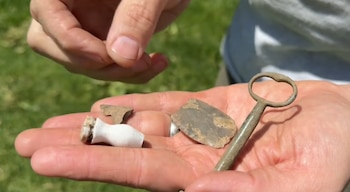 Mano sosteniendo artefactos antiguos: una llave de metal, un fragmento de piedra, una pieza de cerámica blanca y un trozo de metal irregular