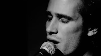 Primer plano en blanco y negro de Jeff Buckley cantando en un micrófono con los ojos semicerrados. Su perfil derecho es visible sobre un fondo oscuro