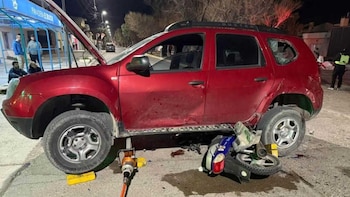 Un automóvil rojo elevado sobre tacos y una motocicleta dañada caída sobre el asfalto junto a herramientas de rescate en la noche