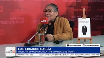 Hombre con gafas y cabello largo gris hablando en un micrófono. En la mesa hay un vaso de agua y un libro en un atril. Fondo rojo con logos de radio