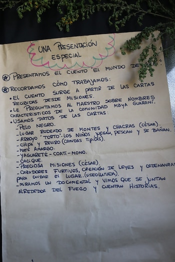 Papel afiche con texto manuscrito en tinta azul y un dibujo decorativo superior, flanqueado por ramas secas en la parte superior derecha