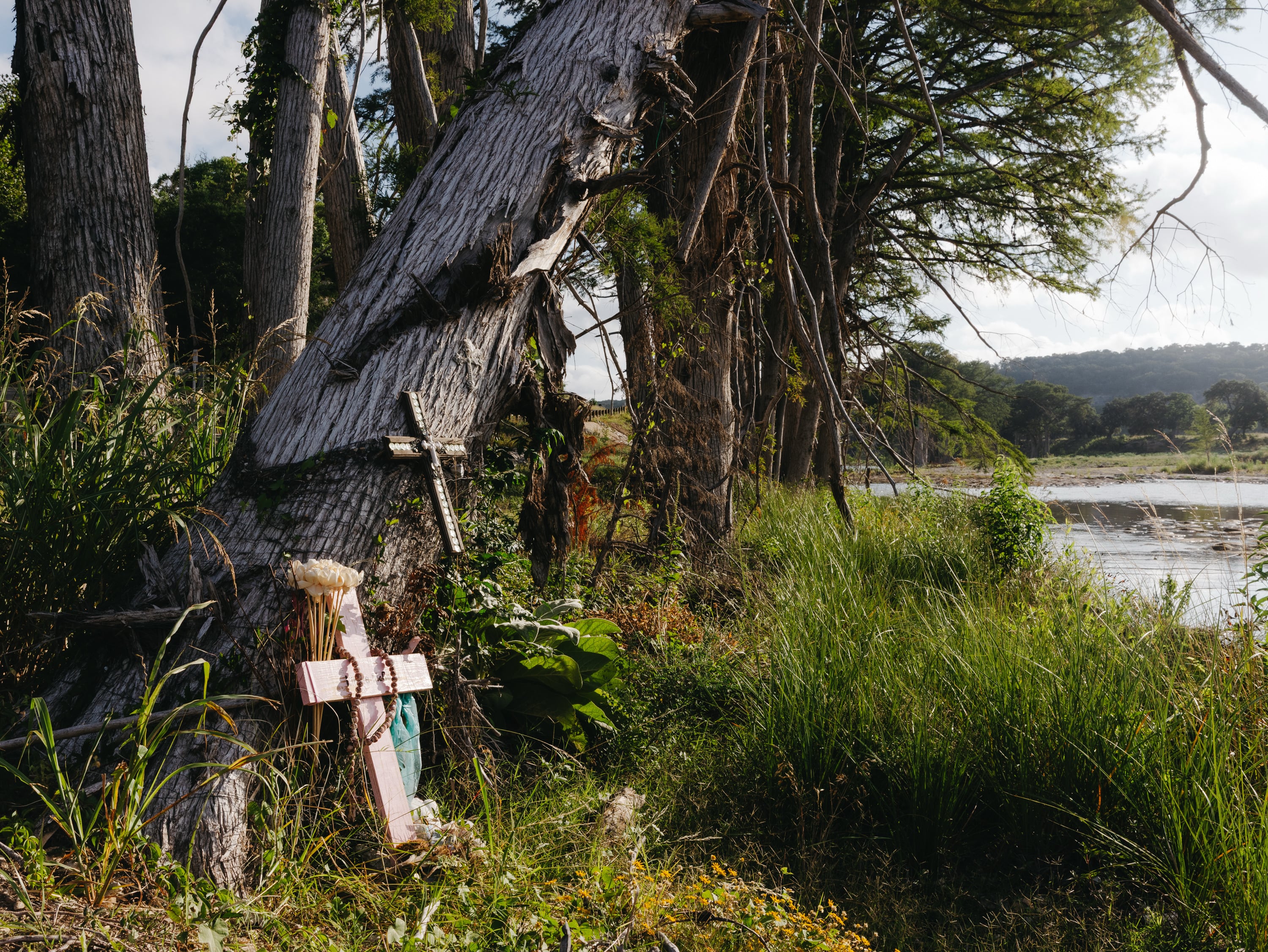 Cruces y ofrendas florales marcan un memorial a orillas del río, rodeado de árboles y vegetación frondosa. (Christopher Lee/The Washington Post)