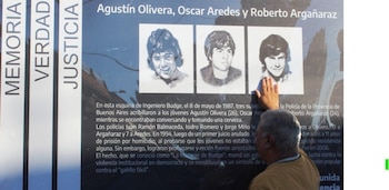 Primer plano de una mano tocando una placa conmemorativa que muestra tres retratos en blanco y negro de jóvenes y texto en español sobre un crimen