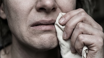 Primer plano de la nariz, la boca y la barbilla de una persona con una mano que presiona un pañuelo de tela claro sobre sus labios.