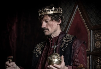 Actor Nikolaj Coster-Waldau de perfil, con bigote, vistiendo una corona dorada y túnica roja con bordados, sosteniendo un orbe y un objeto dorado