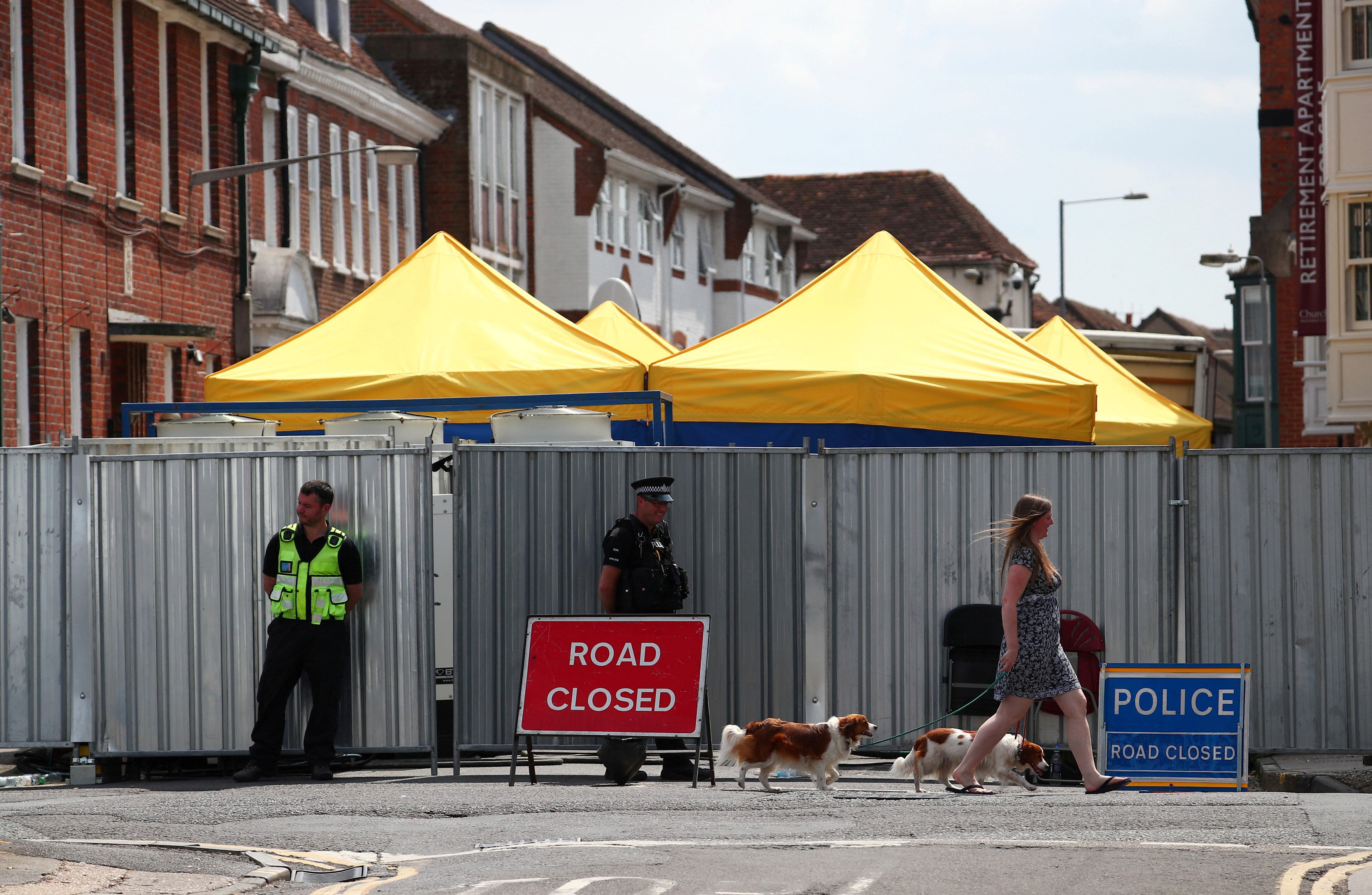 Una mujer pasea a sus perros frente a policías apostados en la calle donde vivía Dawn Sturgess, quien falleció tras ser expuesta al agente nervioso Novichok, en Salisbury, Reino Unido. REUTERS/Hannah McKay