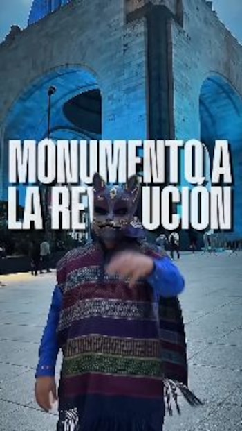 Una persona con poncho y máscara de felino posa frente al Monumento a la Revolución con el texto sobreimpreso Monumento a la Revolución