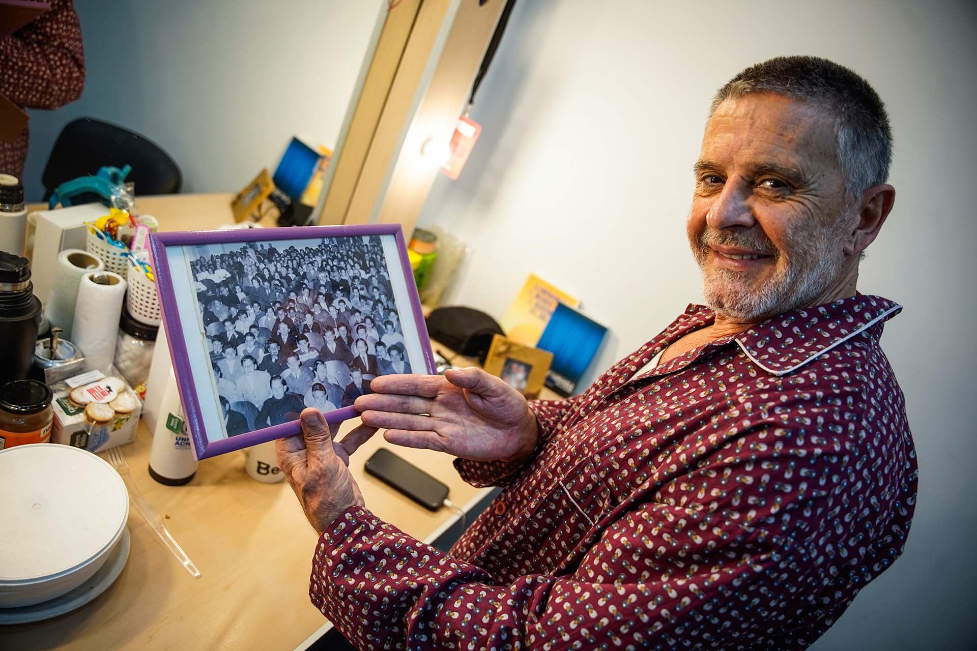 Osvaldo Laport con una fotografía que lo acompaña en todos sus camarines desde que llegó a la Argentina desde Uruguay. La imagen es en el teatro de su pueblo, Juan Lacaze. Él está debajo, de blanco (arriba de su dedo pulgar). A su derecha, sobre su mano, está su hermano Daniel, que era escultor y falleció; en el escenario está Luis, otro de sus hermanos, que es periodista y actor vocacional; y detrás, entre la gente, sus padres (Crédito: RSFotos)