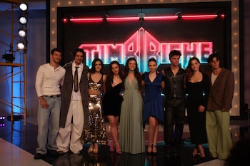 Nueve personas vestidas de fiesta posan alineadas frente a un letrero luminoso de neón que dice Timbiriche en un escenario
