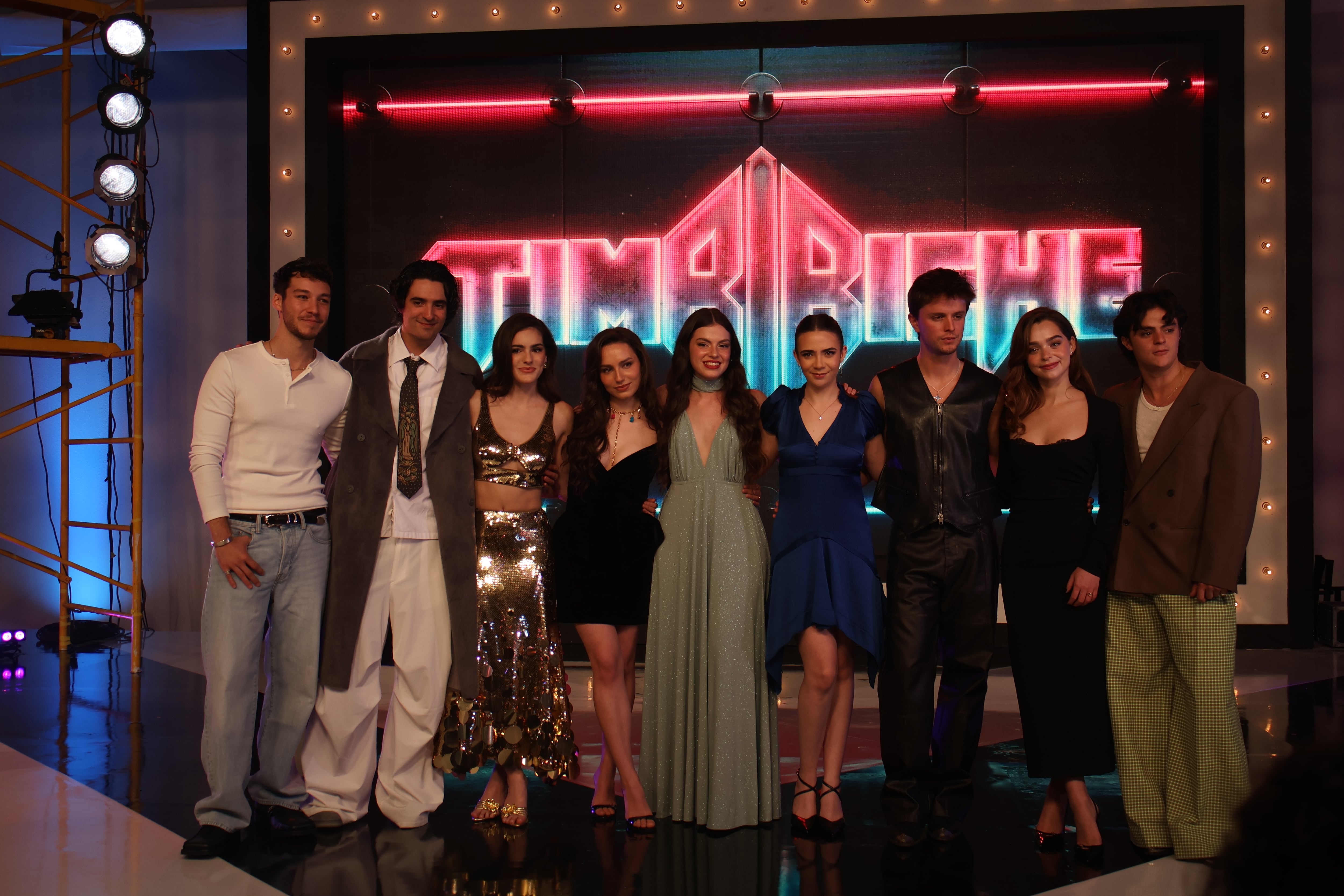 Nueve integrantes del elenco de la producción Timbiriche posan en un foro frente a una pantalla iluminada con el nombre del proyecto. (Infobae México/Selene Miranda)
