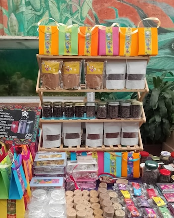 Un puesto de mercado con una estantería de madera. Muestra bolsas de regalo, frascos con granos, paquetes de productos y dulces surtidos