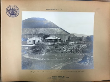 Fotografía en blanco y negro de la Pirámide del Sol en Teotihuacán, con edificios y un jardín paisajístico en el primer plano, y personas trabajando
