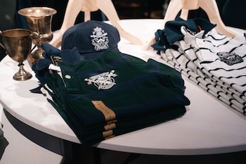 Polos doblados con bordados, una gorra azul marino y dos copas de metal sobre una mesa blanca