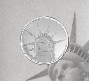 Una moneda circular plateada con el rostro de la Estatua de la Libertad sobre un fondo gris con un grabado del mismo monumento