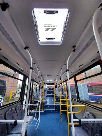 Interior de autobús nuevo con asientos cubiertos, pasamanos amarillos y blancos, piso azul y una claraboya en el techo con el logo Ugarte